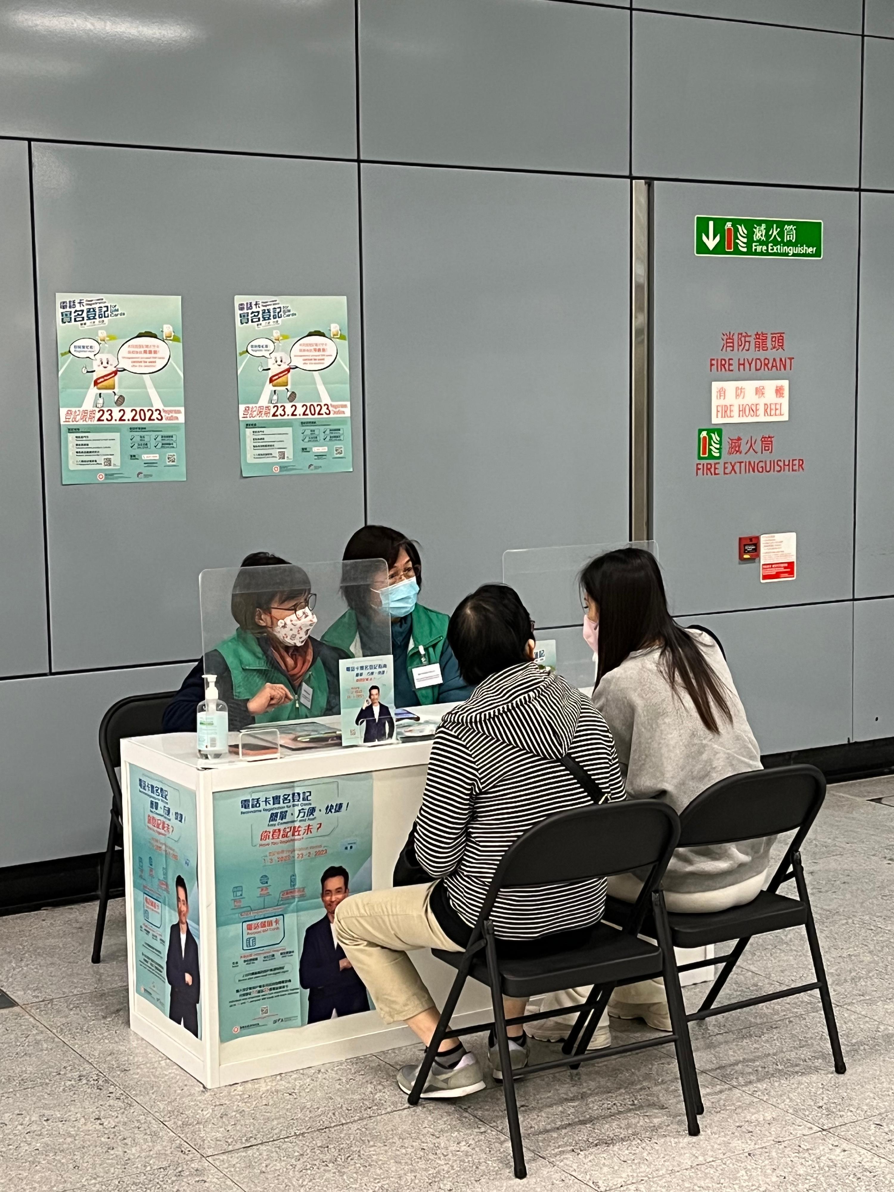 為提升公眾的認知及協助市民進行電話智能卡實名登記，通訊事務管理局辦公室近期推行一系列相關的宣傳活動及便利措施，包括於25個港鐵站加強提供支援服務。圖示支援站人員為市民提供協助。